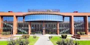 Fachada acristalada de una universidad pública madrileña con jardines, referente de los créditos más caros en España.